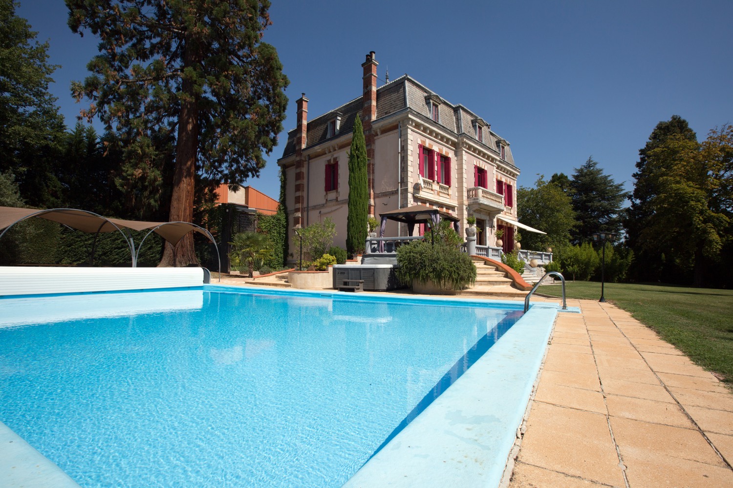 The château seen across the swimming pool, with its giant sequoia and green lawns